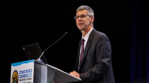 An indoor image of KBHN Chief Scientific Officer Dr. James Reynolds speaking at the podium while cochairing the presidential plenary sessions.