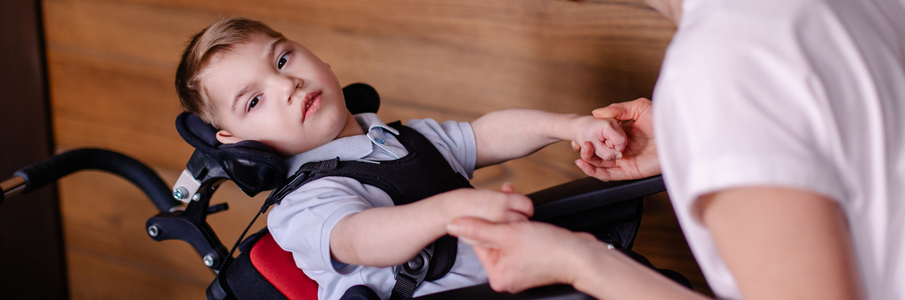 Boy child in a special wheelchair with cerebral palsy helped by his mother.