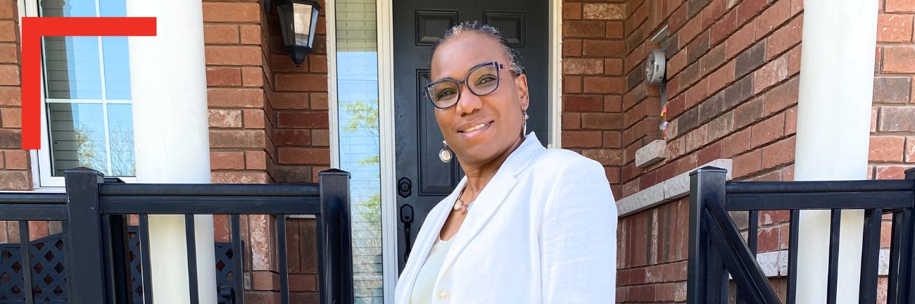 Sheila, a black woman wearing a white blazer, looks on, smiling.