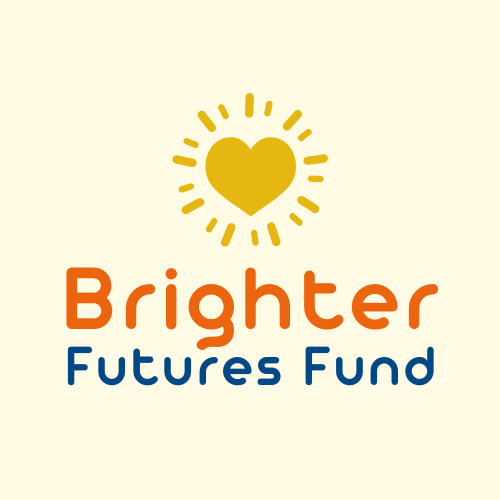 Two young siblings smiling in a park filled with green grass and tree