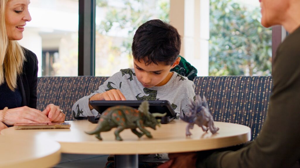 Minister Beech's daughter Nova and KBHN Interim CEO Geoff Pradella look over the Dino Island game on a tablet.